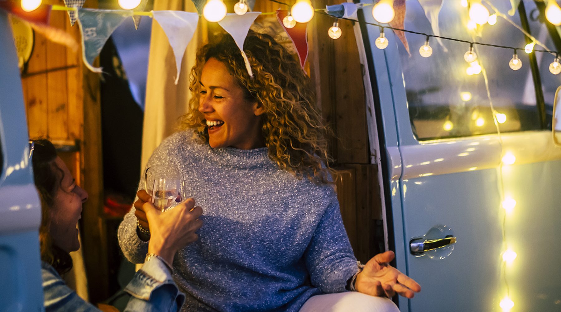 Alternative travel and celebration concept with couple of people adult cheerful happy women celebrate together in a vintage van camper  and party lights outdoor